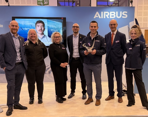 Seven people smile to camera while one holds an award. 