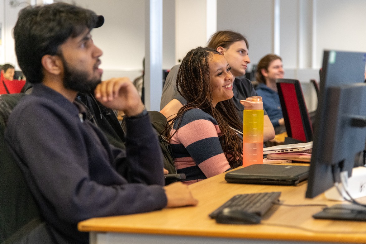 BSc Cyber Security students in one of our computer labs, sat at desks and listening to the lecturer