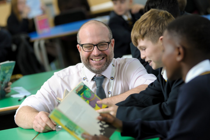 A teacher smiling with two boys reading in the school library