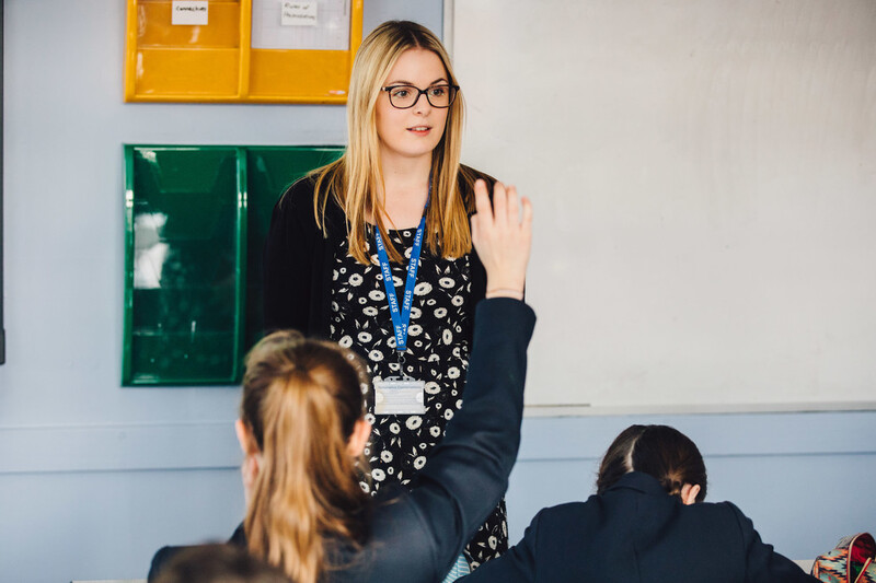 a student raises their hand while a teacher is teaching a class 