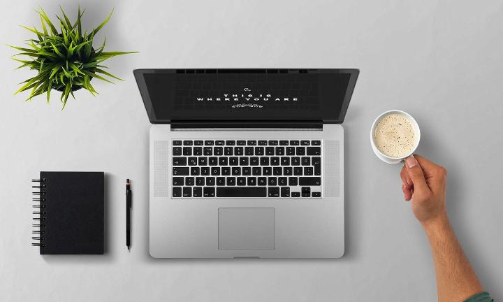 Laptop with notepad and hand holding a drink