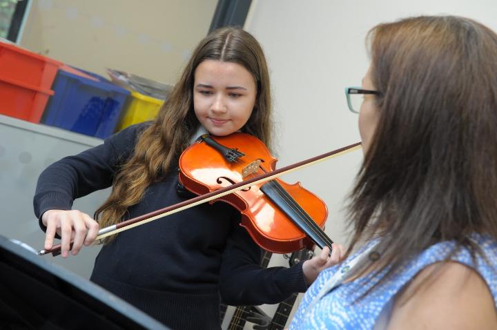 music student playing a violin with the teacher in front