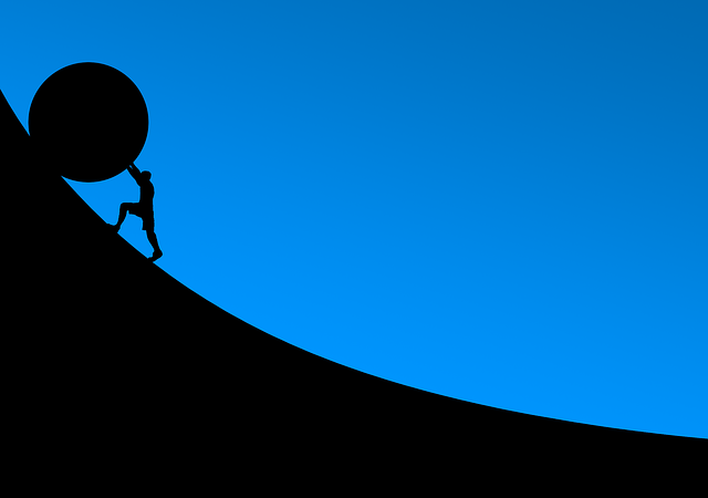 Silhouette of person pushing a stone up a hill 