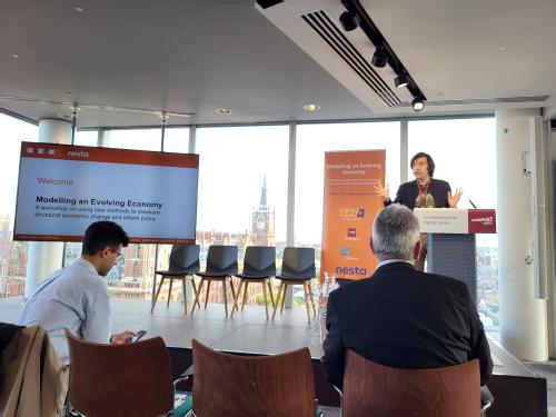 Picture of Mirko Draca presenting at the Modelling an Evolving Economy workshop overlooking St Pancras Station on the Euston Road. He is a white man with long dark hair in his 40s