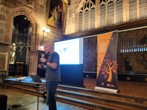 Photo of Omer Moav presenting in the wood, stone and decorative objects surroundings of St Mary's Guildhall in central Coventry. He is a middle aged white man wearing a t-shirt