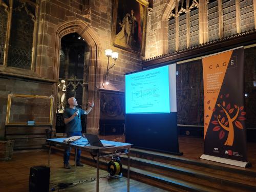 Omer Moav pointing at a projector screen whilst presenting in the wood and stone surroundings St. Mary's Guildhall a 15th Century civic hall in central Coventry