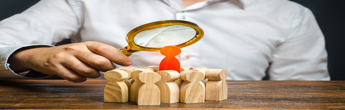 person with magnifying glass studying wooden 3d figures