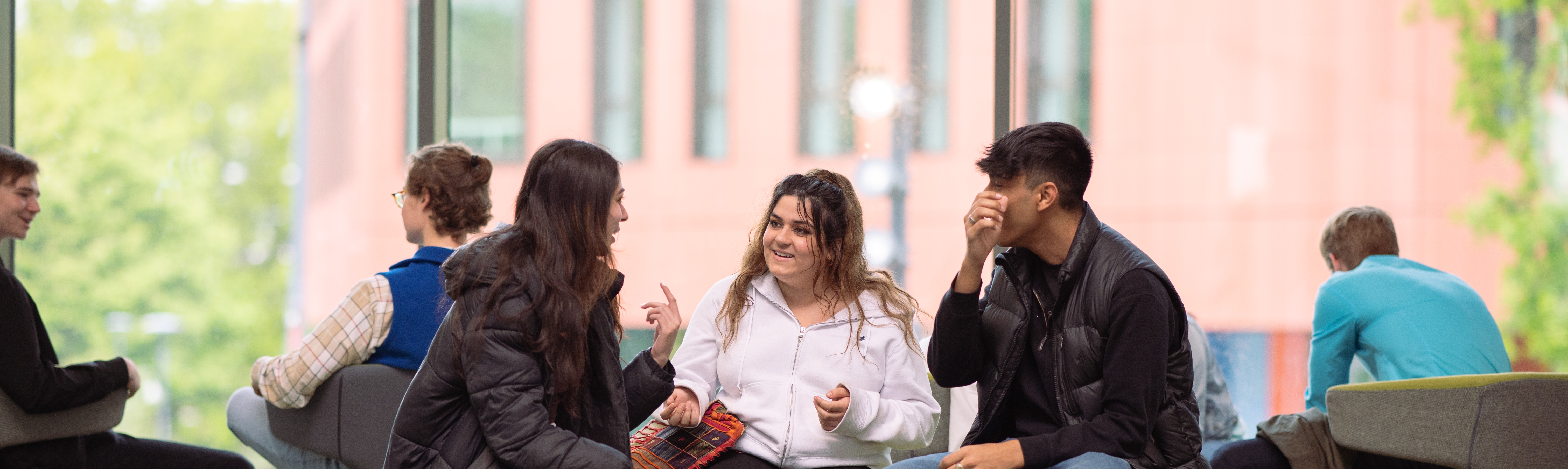 three philosophy students sit at a low table by a window with a view of the Faculty of Arts building in the background