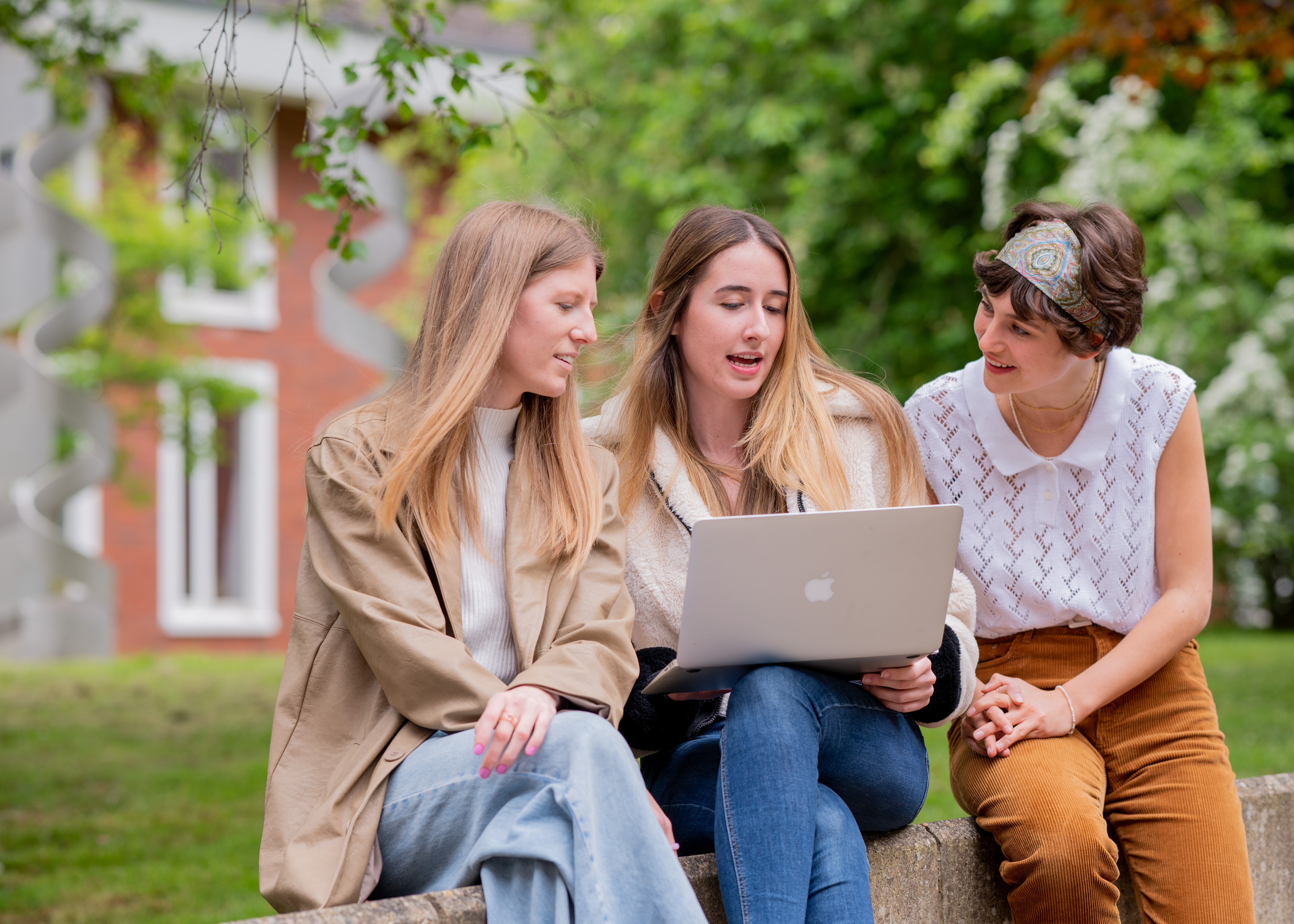 a group of three postgraduate Philosophy students sit on a bench looking at a laptop