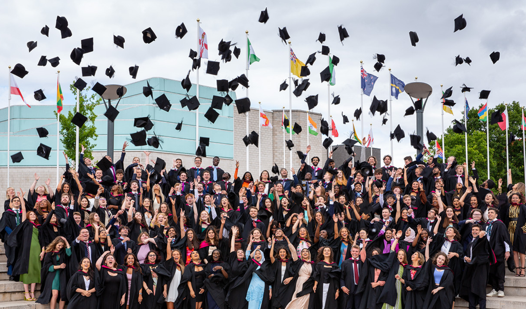 A large group of University of Warwick alumni throwing their caps into the air in celebration.
