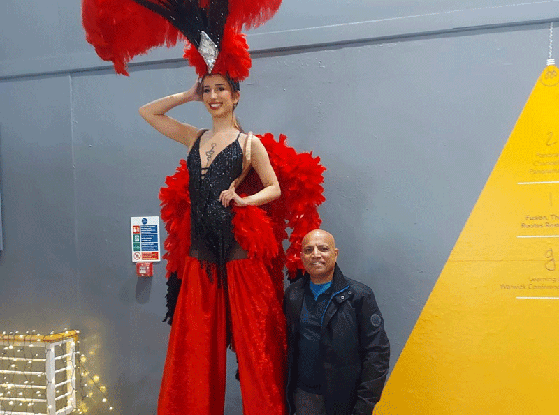 Dilip at staff celebration party next to performer on stilts