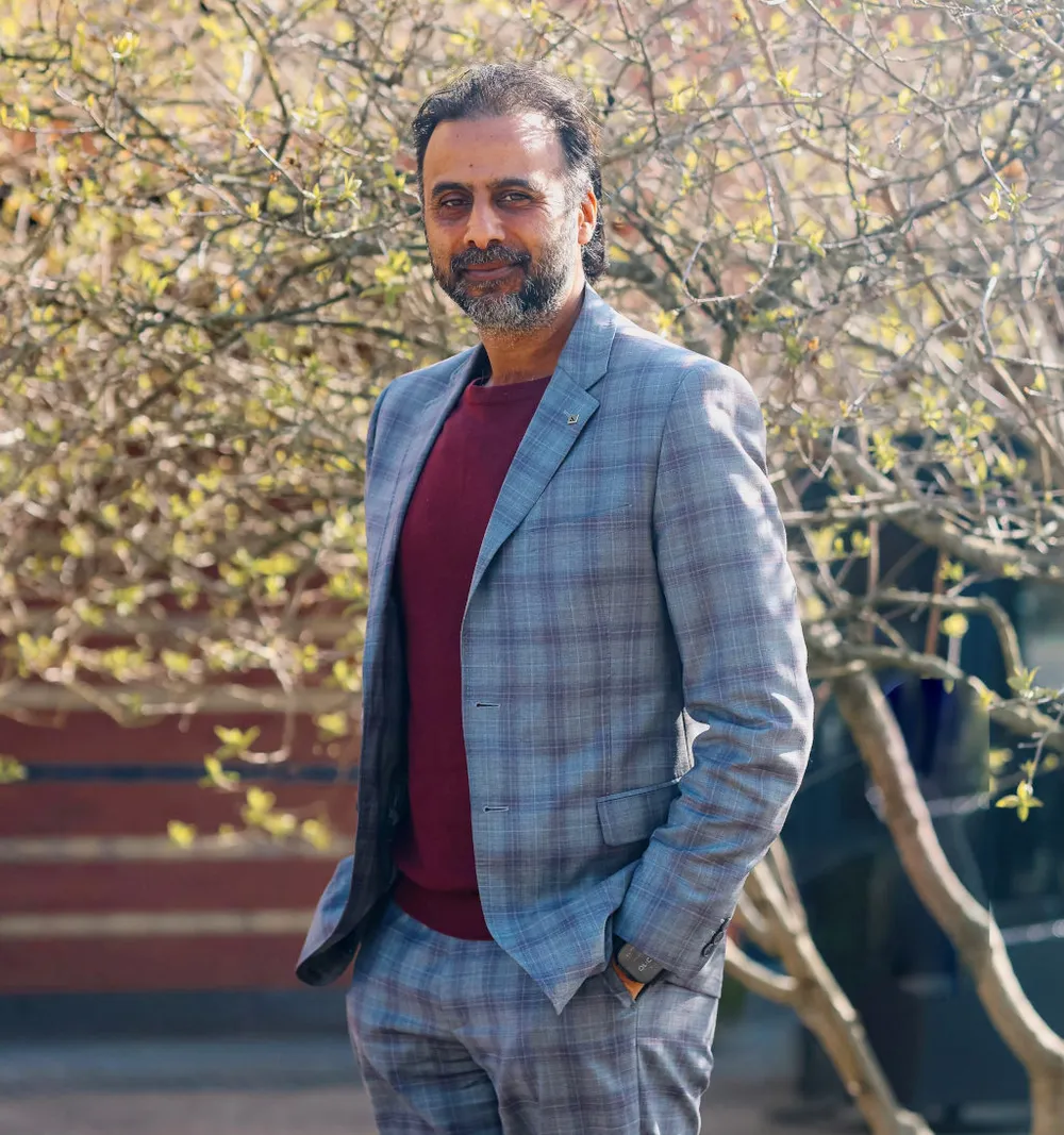 Image of Raja. He is wearing a suit and is smiling, with a tree behind him.
