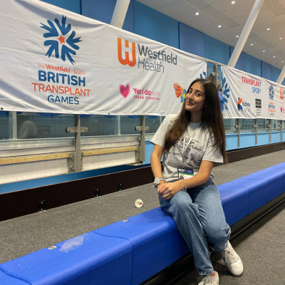 Image of Anika sitting in front of the Transplant Games banner