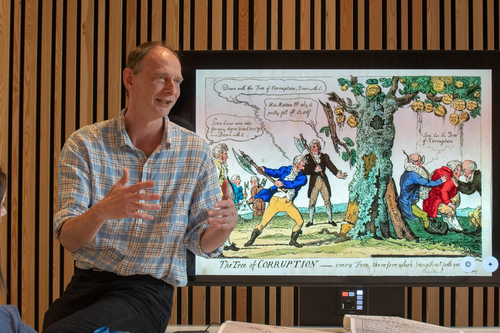 A lecturer teaching with a 'tree of corruption' image shown on screen behind him