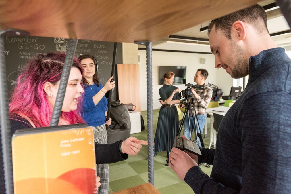 Students using film and audio recording equipment, with a lecturer interacting.