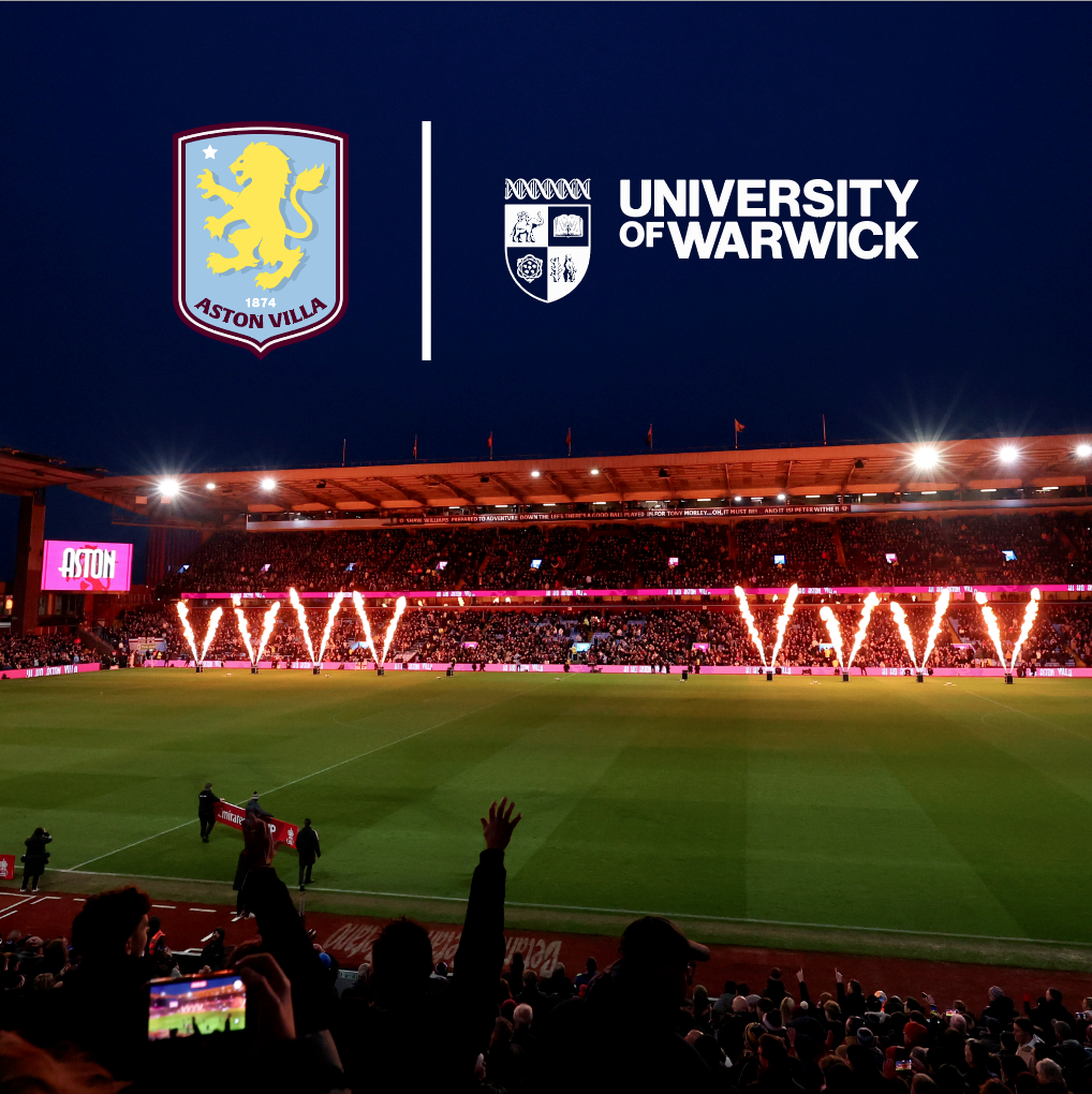 Villa Park at night with flame flares with Aston Villa FC and University of Warwick logos