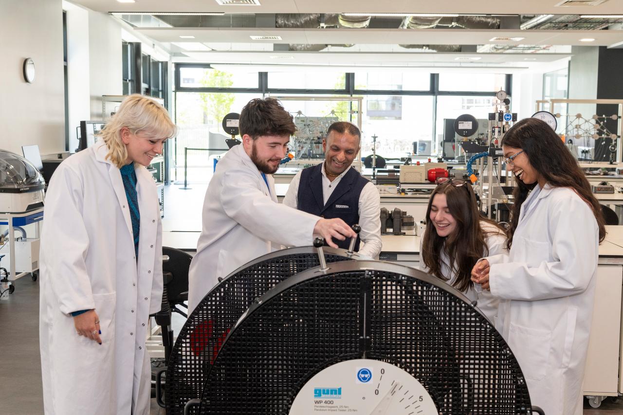 Four apprentices wearing lab coats examining a machine