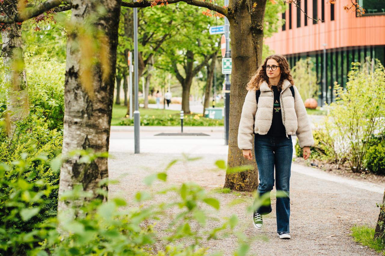 Student walking through trees with the Faculty of Arts Building in the background