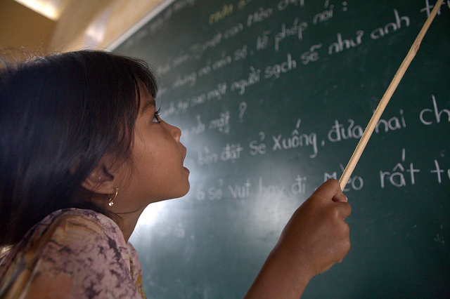 A young girl reads from a blackboard