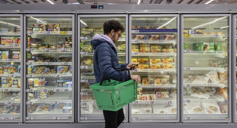A man standing in front of a freezer in a supermarket displaying convenience food
