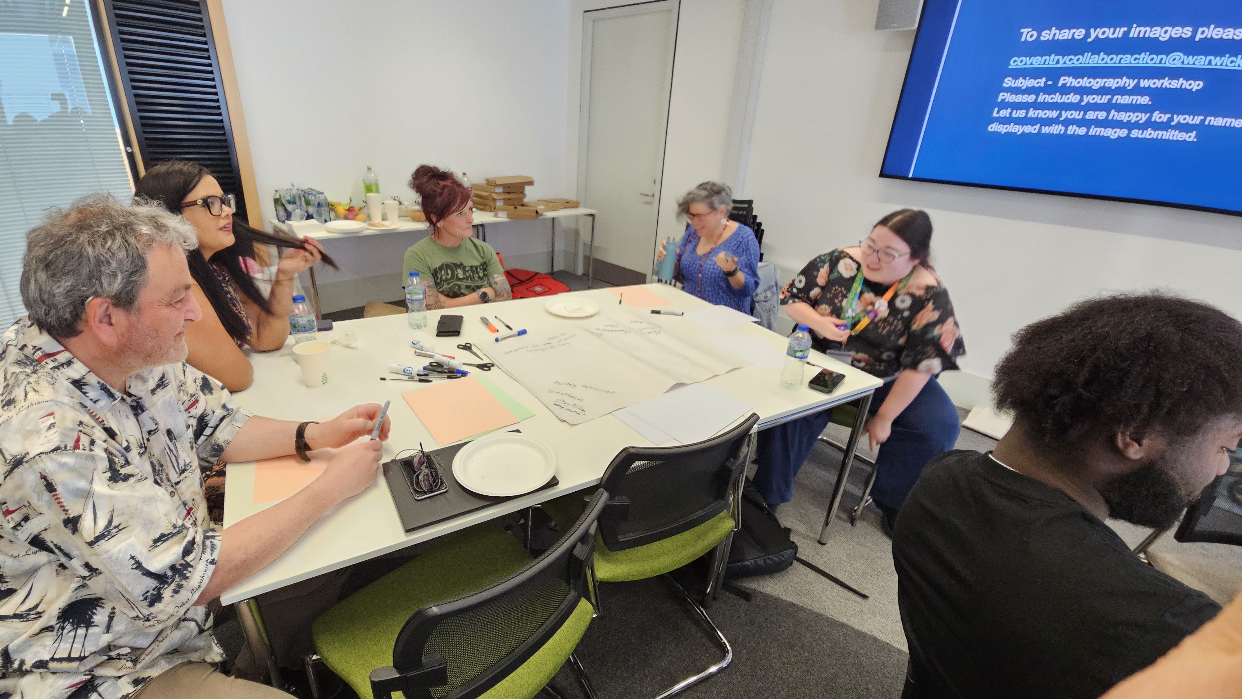 5 people sat around a table at a Drop the Mask workshop discussing neurodivergence and the use of art to communicate experiences and feelings.