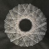 Grey stitching on a black felt fabric background. Some of the stitching is long, loose straight stitching and some is in a zig-zag stitch. The lines cross backwards and forwards to create a circular shape with a hole in the middle, a bit like a ring donut.