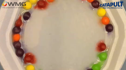 A GIF showing the colour dissolving from sweets into water to make a rainbow pattern.