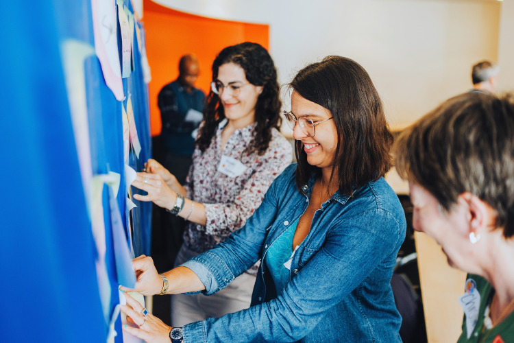 People adding post-it notes onto a communal working board