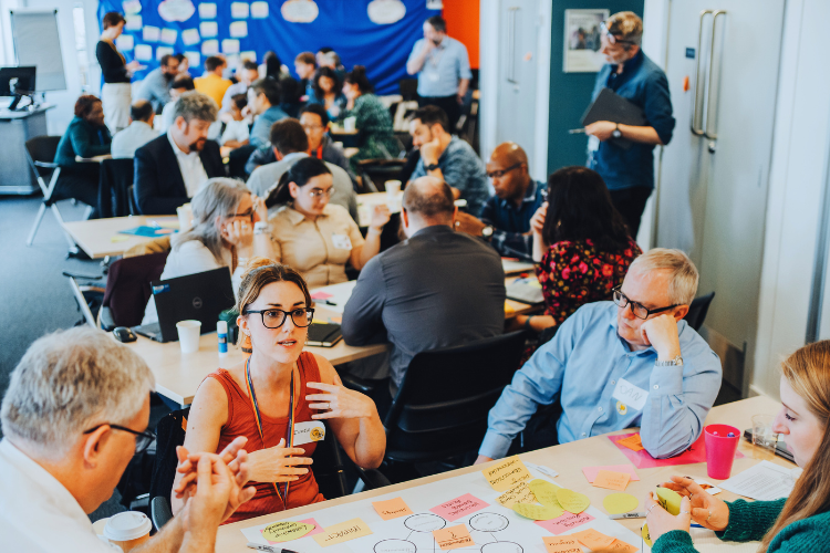 People sat around tables discussing ideas and writing thoughts on post-it notes