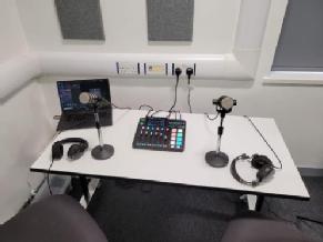 Rodecaster Pro with 2 microphones on small stands and 2 headphones, table is against the wall.