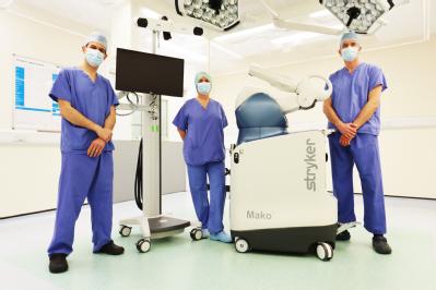 Andy Metcalfe, Elke Gemperle-Mannion (the RACER Trial Manager) and Ed Davis standing with the type of robot that will be used for the study in the theatres of the Royal Orthopaedic Hospital in Birmingham. Credit: Royal Orthopaedic Hospital in Birmingham