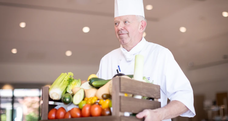 A chef walking holding a crate of fruit and vegetables