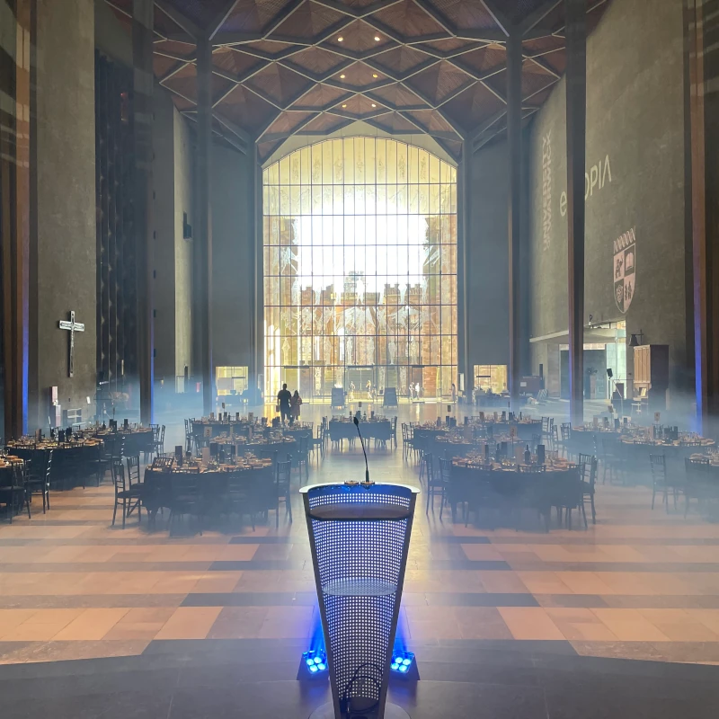 A full view of inside Coventry Cathedral's beautiful architecture, decorated with a plethora of round tables and dining chairs, dressed for an iconic banquet dining experience.