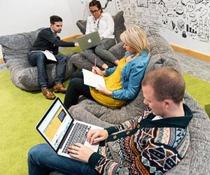 A group of people on comfy beanbag seating working together with graphic doodle decoration on the wall.