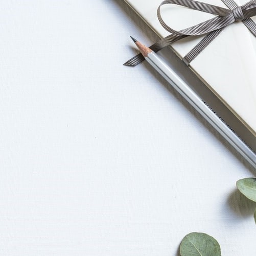 Pencil, leaves and bow tied paper against white background