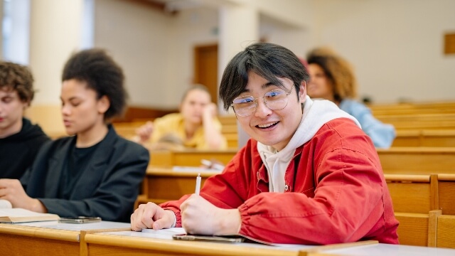 Male student in a red jacket sitting at the table and smiling