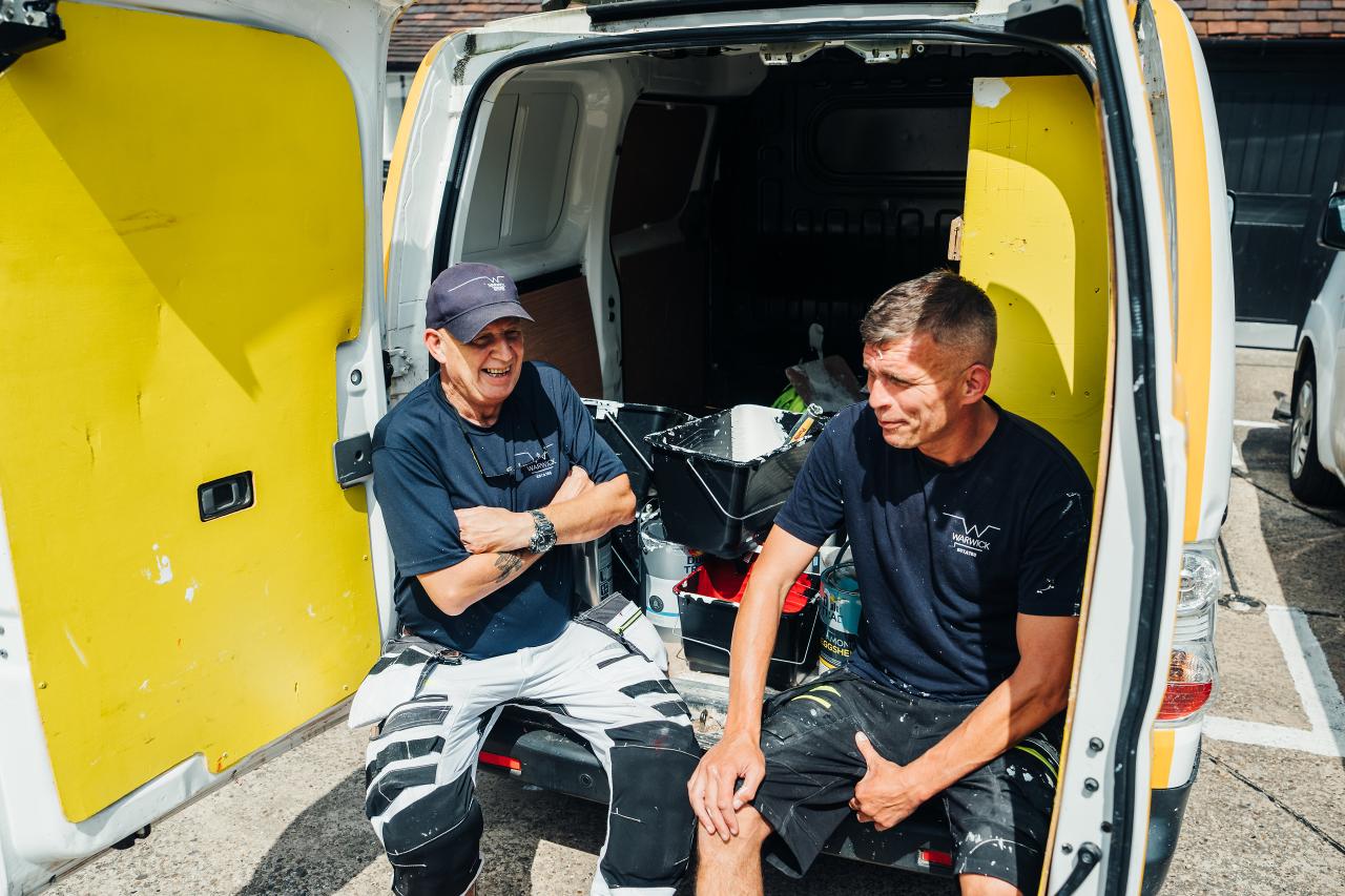 Two men seated in the back of a service van with work equipment