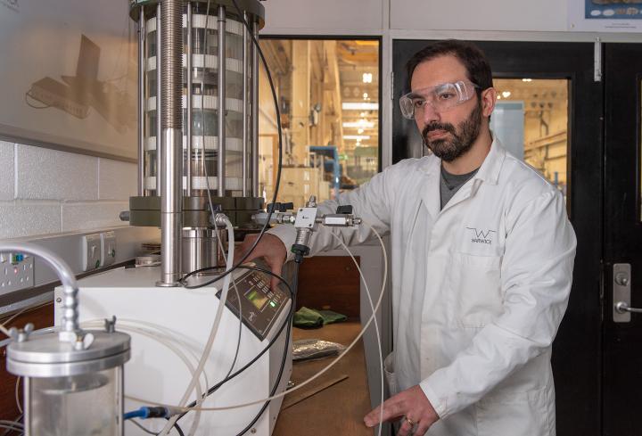 A man in a lab coat and protective eyewear with some mechanical equipment