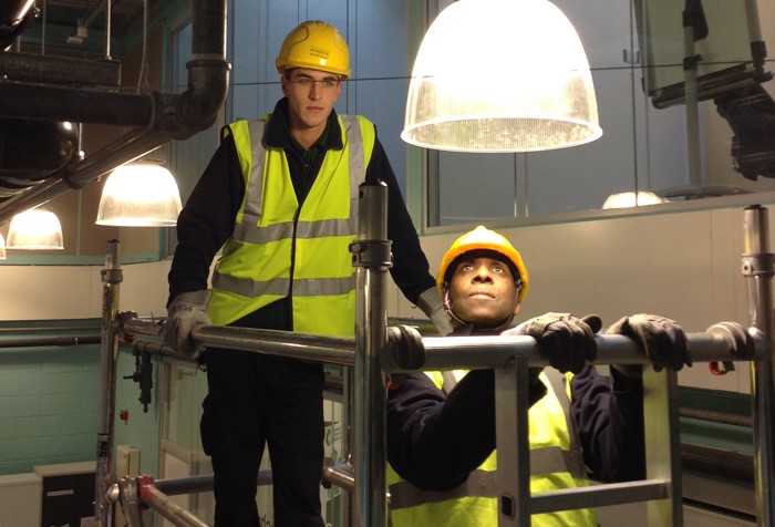 Electrical engineers inspect a light fitting wearing hard hats and high visibility vests