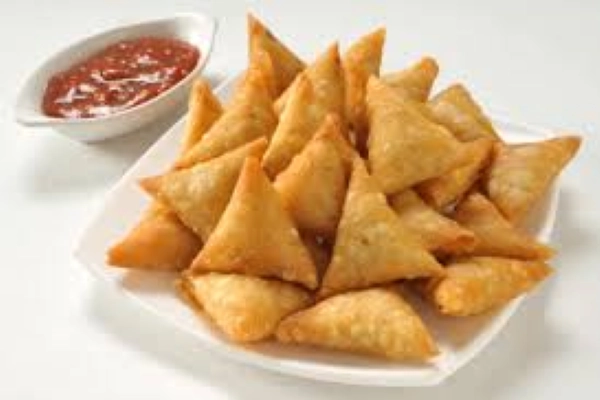 A bowl of samosas with chutney beside it