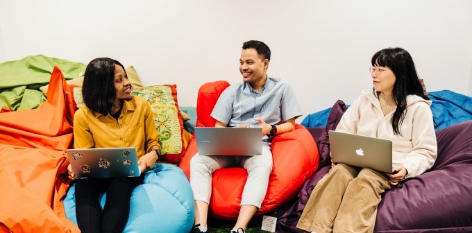 3 students sitting on bean bags, with laptops. They are all smiling