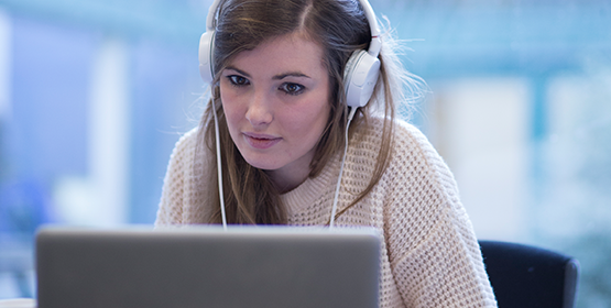 A woman, wearing headphones, looking at her laptop