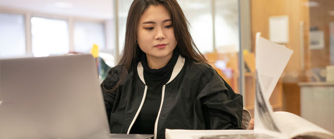 Student working with a laptop and book in the Library