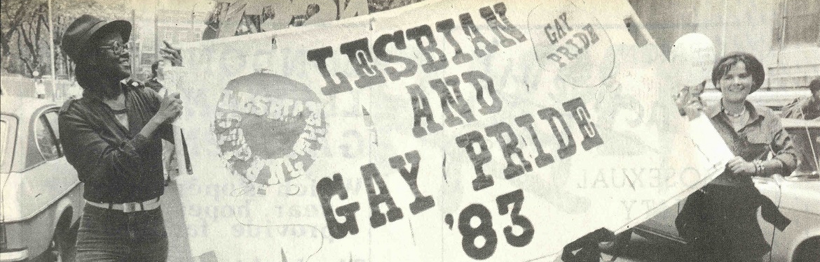 Photograph of two people carrying a banner with the caption 'Lesbian and Gay Pride '83'