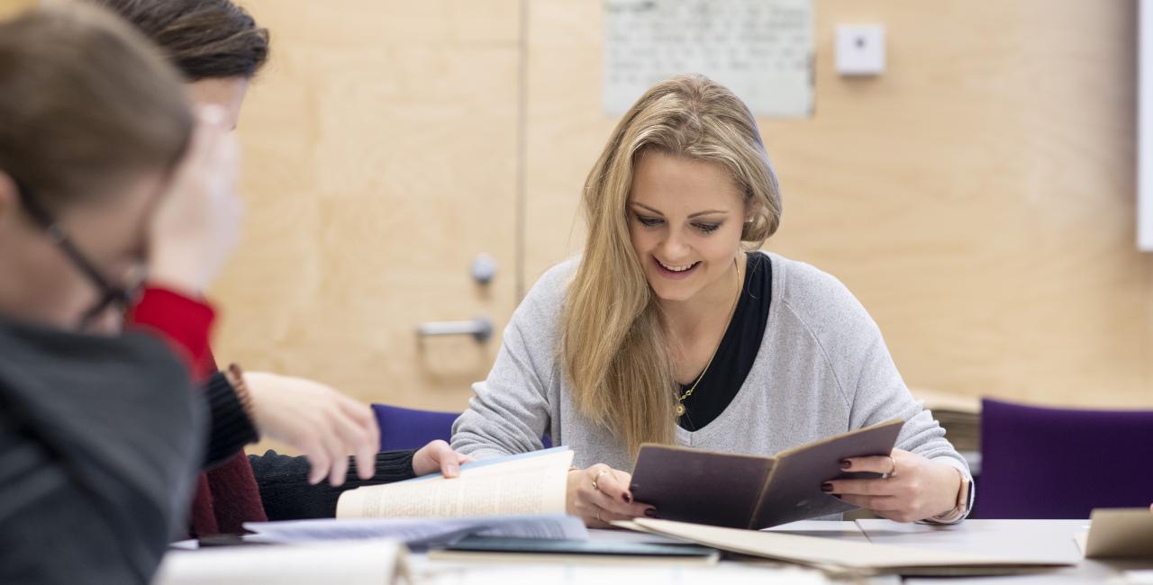 Photograph of a student study session, focusing on a student looking through a small archival volume.