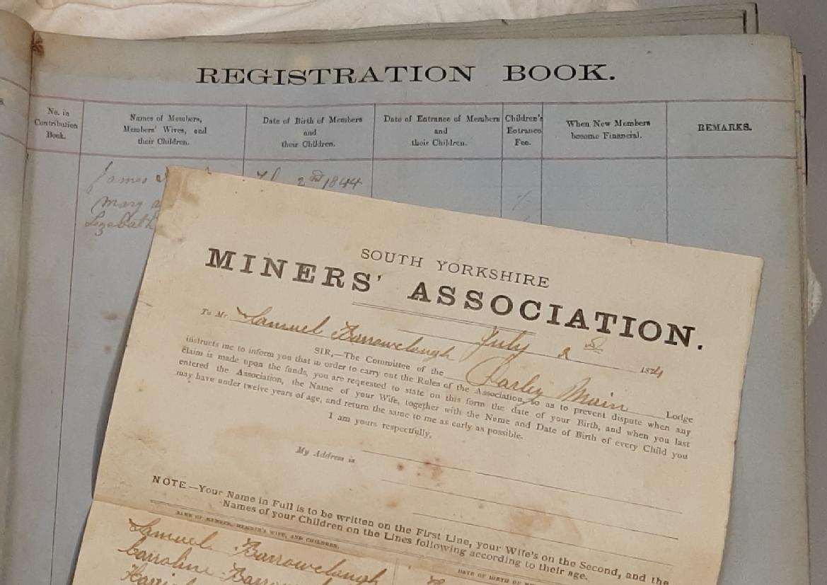 Photograph of part of a membership register belonging to the South Yorkshire Miners' Association, a form submitted by a member is lying across the open page.