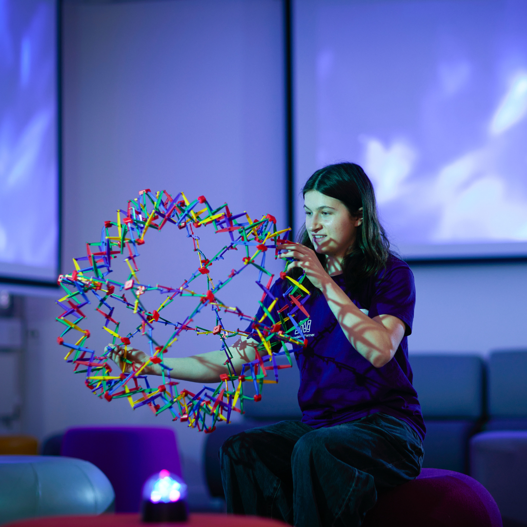 A Library Student Partner holding a sensory toy which expands. Blue lighting making the photo look like a calming sensory environment.