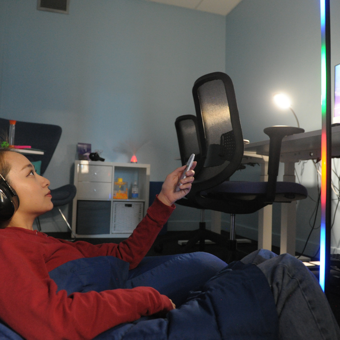 Photo of a student using an accessible study room with ear defenders on, sitting on a bean bag and changing the lighting.