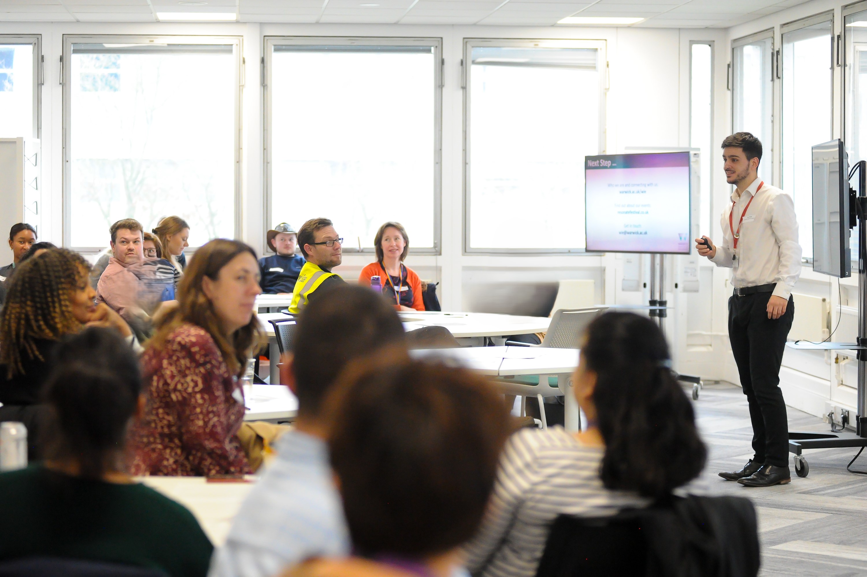 A facilitator standing at the front talking to a room of people 