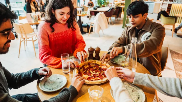Four people sitting around a table in a restaurant sharing a pizza.